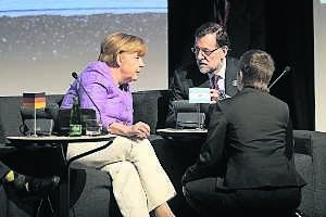 Merkel y Rajoy, sentado en una mesa de la delegación argentina, conversan durante la breve reunión que mantuvieron ayer en Santiago de Chile. ::
PABLO OVALLE / EFE/